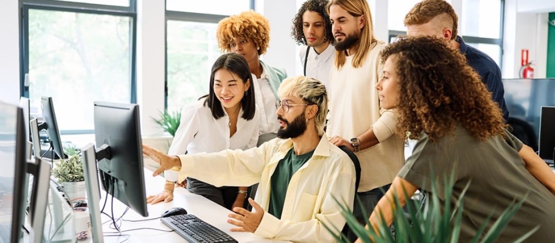 Young man showing data and explaining something to colleagues in a meeting in front of the computer in a coworking